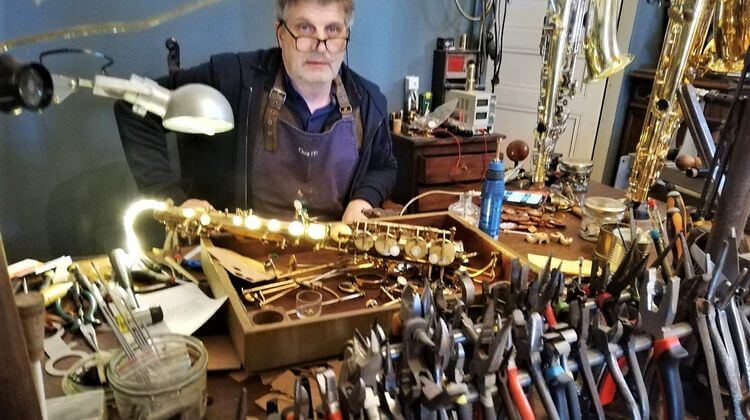 Martial Maigret derrière son établi dans son atelier, en train de réparer un saxophone