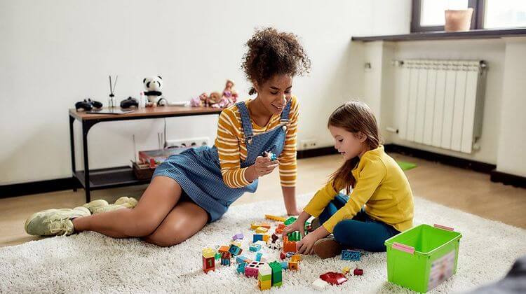 Une jeune fille en train de jouer aux cubes avec une enfant sur un tapis