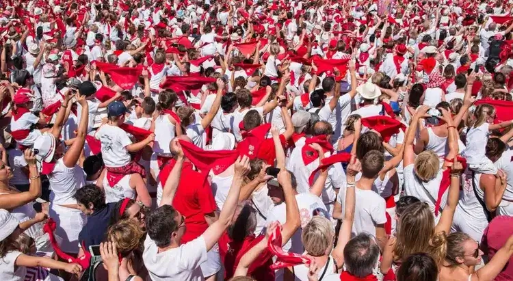 Une foule habillée en rouge et blanc brandit des foulards rouge en l'air.