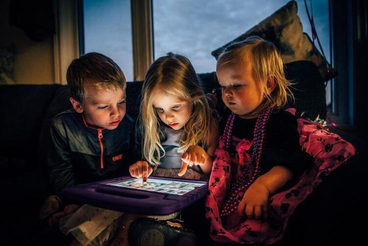 Trois enfants regardent un écran.