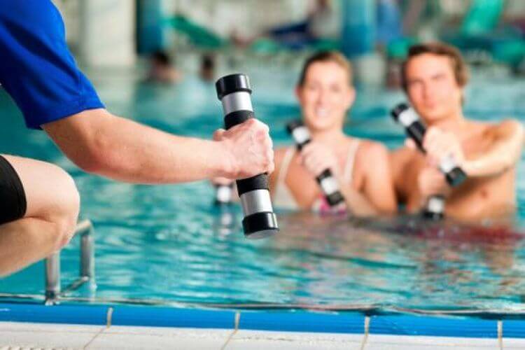Un couple tient un appareil de musculation dans une piscine.