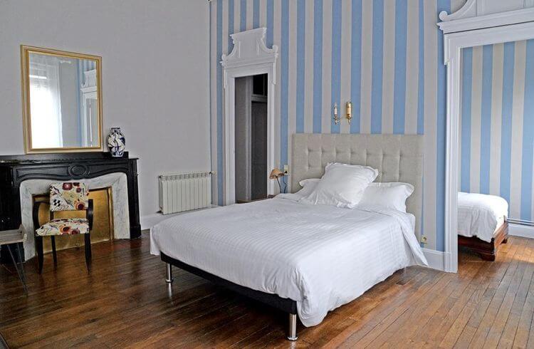 Une chambre avec parquet ciré, belle cheminée, grand miroir, tapisserie bleue et blanche à rayures