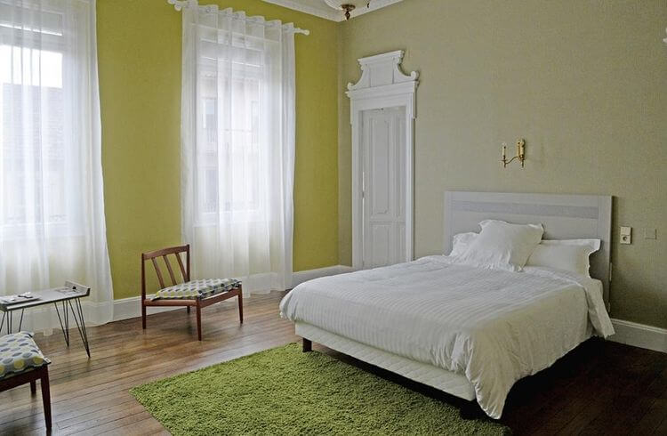 Une chambre jaune pâle et beige, parquet ciré, grand tapis, grand lit et fauteuils