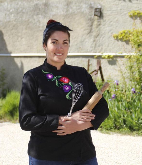 Nadège Blasig tenant dans ses mains un rouleau et un fouet à pâtisserie dans une cour extérieure