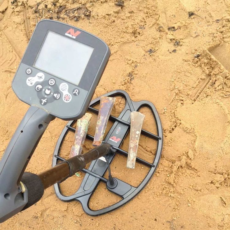 Un détecteur de métaux sur le sable, avec des haches en bronze.
