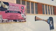 Le mur de la halle au gras de Gimont avec le panneau indiquant Les Grasses matinées, et un dessin sur la façade représentant un enfant avec un long masque de canard