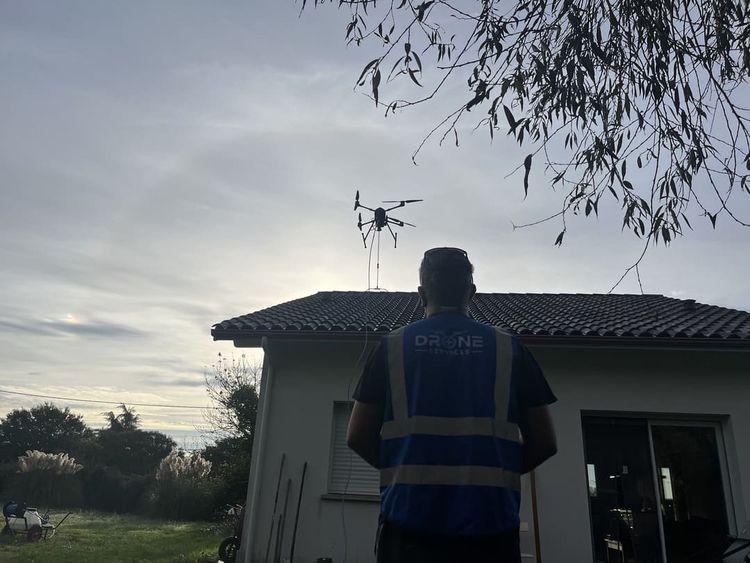 Un pilote de drone devant une maison au dessus de laquelle vole un drone de nettoyage.