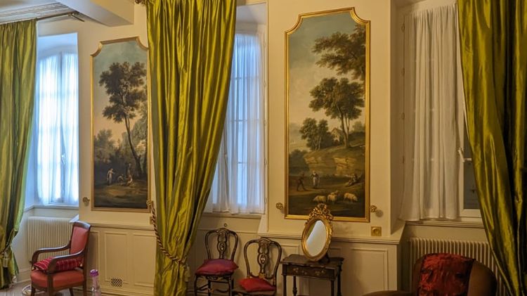 Un salon rénové avec de grands drapés verts aux fenêtres, trumeaux et chaises dans le style Louis XV