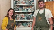 Alexandra et Raphaël Lalanne en tablier de peinture posent devant un vaisselier rénové