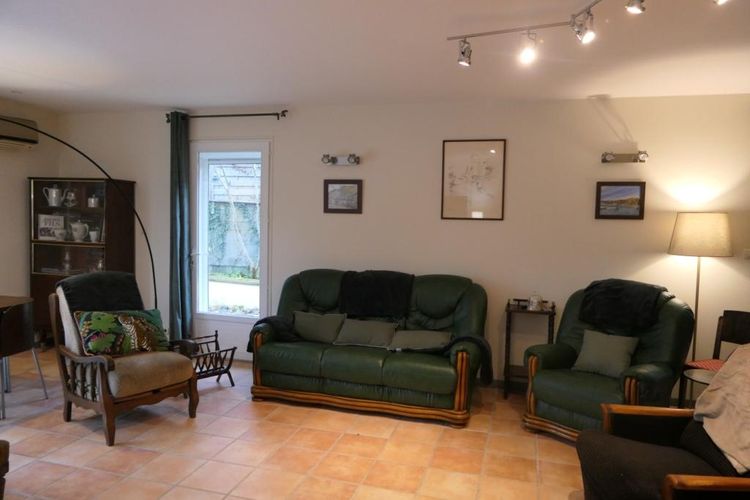 Le salon avec grand canapé et fauteuils, un vaisselier avec cafetières et théières et des tableaux aux murs
