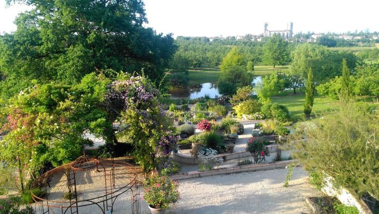 Une autre vue sur La Romieu depuis les Jardins de Coursiana, avec au premier plan une tonnelle, des arbres, arbustes, un lac