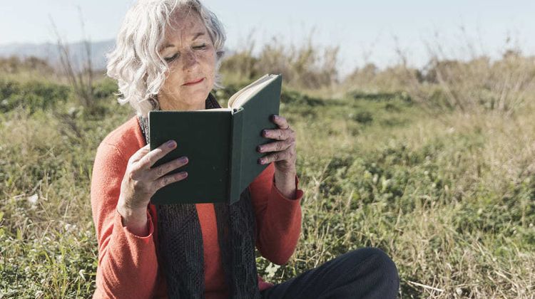 Une femme âgées lit un livre dans un champs. Crédit photo : Freepik