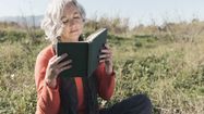 Une femme âgées lit un livre dans un champs. Crédit photo : Freepik