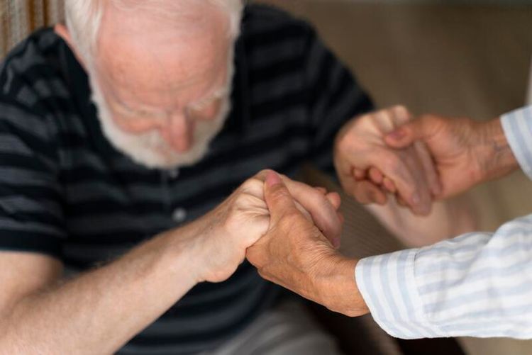 Un sénior essayant de se relever avec l'aide d'une autre personne.